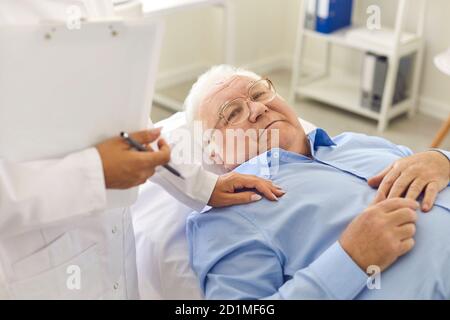 Entspannter älterer männlicher Patient, der im Krankenhausbüro auf dem Bett liegt Während der medizinischen Kontrolle Stockfoto