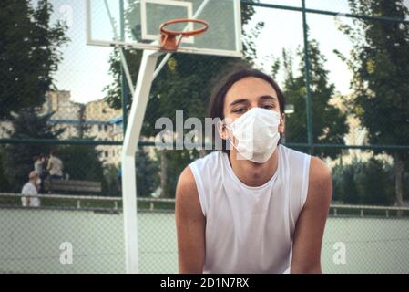 Langhaarige Teenager trägt eine Schutzmaske vor ruhen Des Basketballkorbs Stockfoto