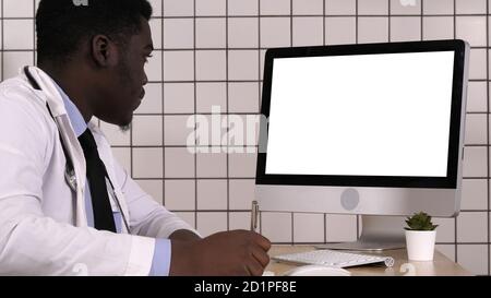 Junger afrikanischer Arzt in einem Laborkittel, der in ihm sitzt Büro und Tak Stockfoto