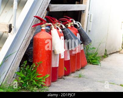 Mehrere alte rote Feuerlöscher stehen in einer Reihe an der Wand auf der Straße. Löschmittel. Brandschutz. Stockfoto