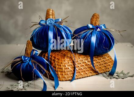 Schöne blaue Kürbisse aus Samtstoff sind mit verschiedenen Elementen und Bändern in einem kleinen Korbkorb verziert. Heimdekor für Halloween Stockfoto