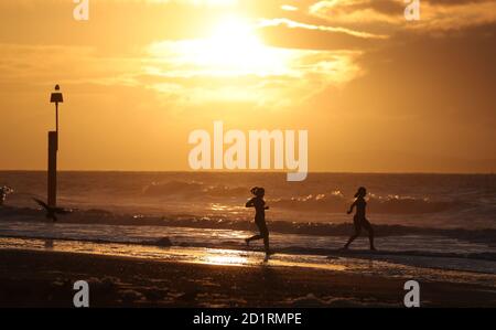 Zwei Schwimmer laufen ins Meer, als die Sonne über dem Strand von Boscombe in Dorset aufgeht.