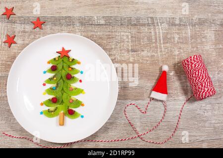 Weihnachtsbaum aus Kiwi-Scheiben auf Holztisch. Kreative Idee für Weihnachtsfrühstück oder Silvester festliche Desserts für Kinder. Draufsicht. Stockfoto