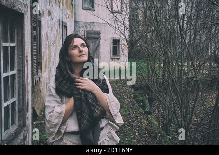 Eine junge Frau schaut in den Himmel und träumt dagegen Der Hintergrund von alten Häusern und Herbstlandschaft Stockfoto