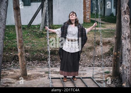 Brunette Frau in Vintage-Kleidung schwingen auf ihren Füßen auf einer Schaukel. Altstadt und Straße mit herbstlichen Blättern Stockfoto