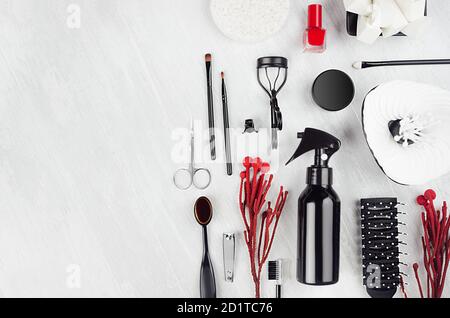 Kollektion von Beauty-Produkten, Make-up-Tools in stilvoller schwarzer Farbe mit rotem Zweig, silberne Pailletten Geldbörse auf weichem hellweißen Holzbrett mit Kopie sp Stockfoto