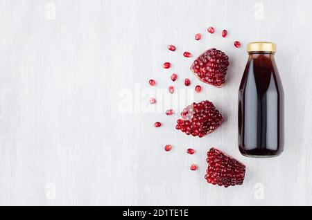 Leuchtend roter Granatapfelsaft in Glasflasche mit Goldkappe, geschnittenes Obst auf weißem Holzbrett, Draufsicht, Kopierraum, Schablone für Design, Werbung Stockfoto