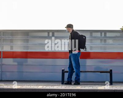 Moskau. Russland. Oktober 2020. Auf der Bahnhofsplattform steht ein einesiger Mann mit Rucksack in einer schützenden medizinischen Maske, der darauf wartet Stockfoto