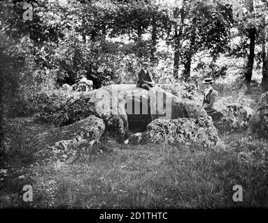 WAYLANDS SCHMIEDE, Ashbury, Oxfordshire. Der neolithische Kammkarren, vom Westen genommen, mit einer Dame und einem Herrn, der auf den Steinen beim Eingang saß. Dies zeigt den Standort weit vor seiner Restaurierung nach Ausgrabungen in den 1960er Jahren. Fotografiert von Henry Taunt (aktiv 1860 - 1922). Stockfoto