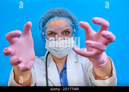Das erschreckende Aussehen eines Arztes mit aggressiv ausgestreckten Händen. Eine Krankenschwester in einem weißen Mantel und Schutzmaske streckt ihre Hände zum Patienten, Stockfoto