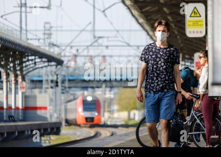 Moskau. Russland. Oktober 2020. Ein junger Mann, der eine medizinische Schutzmaske trägt, geht mit einem ankommenden Zug auf dem Bahnsteig eines Bahnhofs entlang Stockfoto