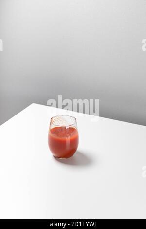 Minimale kreative Komposition mit einem Glas Tomatensaft auf dem Tisch. Geometrisches Kunstkonzept Stockfoto