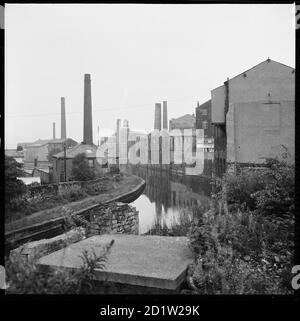 Ein Blick nach Südosten entlang des Leeds und Liverpool Canal von Westgate Bridge zeigt Mühlen und Lagerhallen säumen den Kanal und Clock Tower Mills in der Ferne, Burnley, Lancahire, Großbritannien. Stockfoto