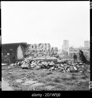 Ein Junge, der durch das abgerissene Mauerwerk der Friedhofmauer in der St Mary's Church mit Gebäuden auf Mabgate im Hintergrund und modernen Bürogebäuden im Stadtzentrum in der Ferne, St Mary's Street, Quarry Hill, Leeds, Großbritannien, geht. Stockfoto