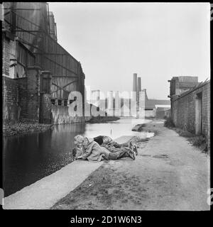 Kinder liegen auf dem Treidelpfad mit Blick in das Wasser des Caldon-Kanals gegenüber der Elektrizitätswerke mit Trent Works und Westwood Mills im Hintergrund, Caldon Canal, Joiner's Square, Hanley, Stoke-on-Trent, Staffordshire, Großbritannien. Stockfoto