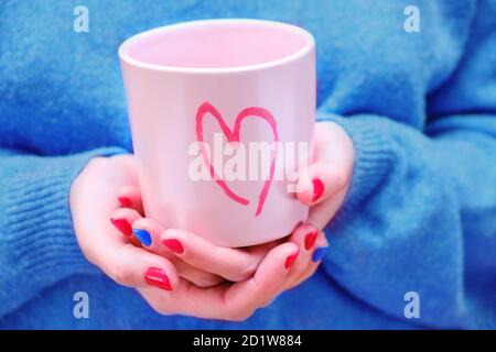 Eine Frau in einem blauen Pullover hält einen rosa Becher Mit einem Herz darauf gemalt Stockfoto