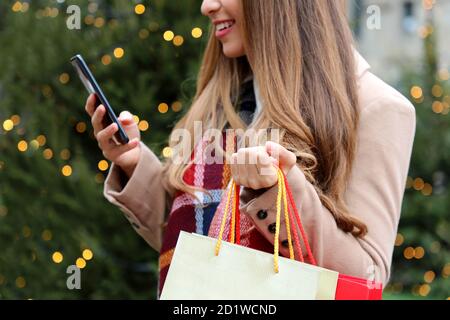 Schöne junge Frau mit mobioe Telefon zum Online-Shopping und Tragetaschen zur Weihnachtszeit Stockfoto