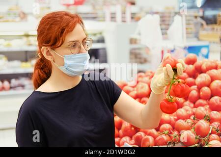 Eine Frau in einer medizinischen Maske wählt Tomaten in einem Supermarkt Stockfoto