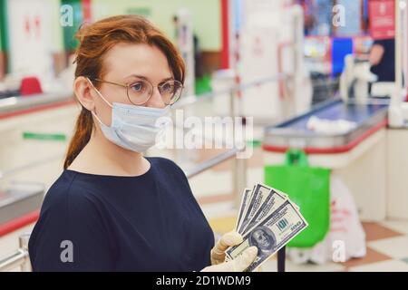 Ein Kunde in einer medizinischen Maske steht mit Dollar in Seine Hände in der Nähe des Supermarktkassensaus Stockfoto