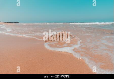 Eine Welle fließt um einen Felsen, an einem Strand im Meer von Asdod, Israel Stockfoto