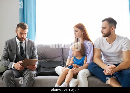 Immobilienmakler kam zu Hause zu verheirateten Paar, sitzen sie diskutieren mögliche bekommen von Hypothek, sitzen auf dem Sofa zu Hause Stockfoto