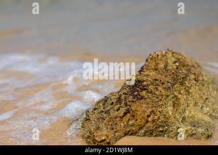 Eine Welle fließt um einen Felsen, an einem Strand im Meer von Asdod, Israel Stockfoto