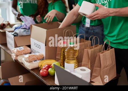 Gruppe von verschiedenen Menschen sortieren durch gespendete Lebensmittel Gegenstände während Freiwilligenarbeit in der Gemeinschaft, verwenden sie Kartons für das Sammeln von Spenden Stockfoto