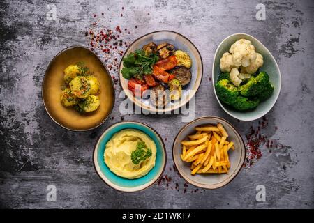 Verschiedene Beilagen auf grauem Hintergrund, Pommes Frites, Kartoffelpüree, Reis, Gemüse, Draufsicht Stockfoto