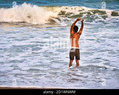 PUDUCHERRY, INDIEN - DEZEMBER CIRCA, 2018. Unidentifizierte männliche Silhouette im Meerwasser an einem Sandstrand. Junge Erwachsene am Strand - schöner Rücken Stockfoto