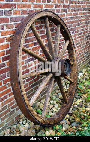 Alte hölzerne Wagenrad mit eiserner Felge. Es ist gegen die Wand zur Dekoration platziert. Stockfoto