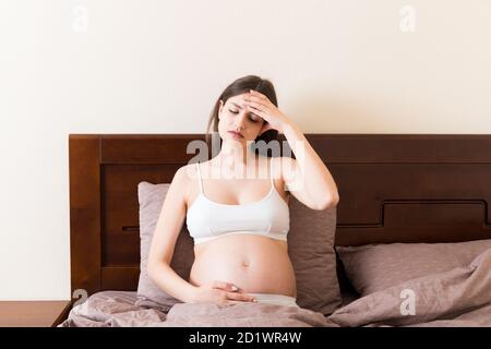 Junge hübsche schwangere Frau mit Kopfschmerzen zu Hause im Bett. Stockfoto