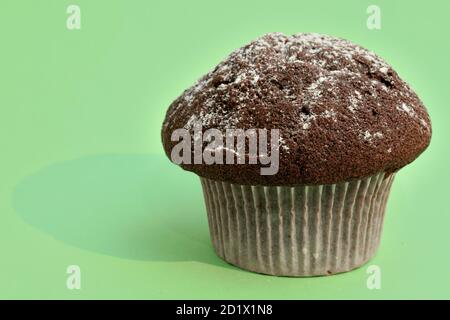 Schokoladenmuffin mit Puderzucker-Nahaufnahme auf grünem Hintergrund verziert. Stockfoto