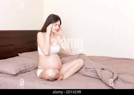 Junge hübsche schwangere Frau mit Kopfschmerzen zu Hause im Bett. Stockfoto