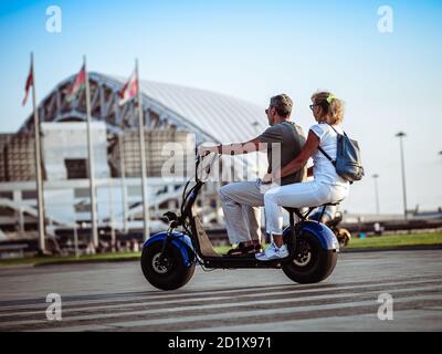 Sotschi, Russland - 16. September 2020: Mann und Frau auf einem zweisitzigen Elektroroller im Olympiapark. Modernes elektrisches Transportkonzept Stockfoto