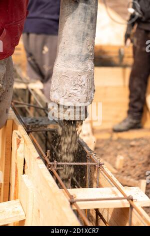 Nahaufnahme von Bauarbeitern, die Zement oder Beton mit automatischer Pumpe in die Fundamentschalung legen. Gebäude Haus Fundament Stockfoto