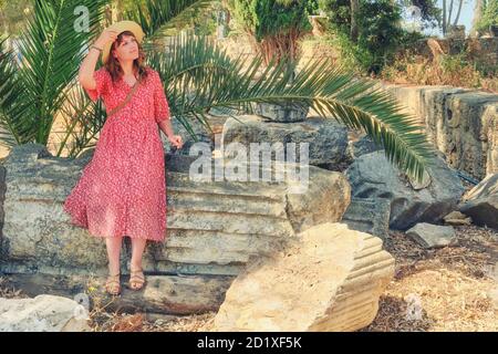 Eine junge Frau in einem Hut sitzt auf einer antiken römischen Säule in Karthago, Tunesien Stockfoto