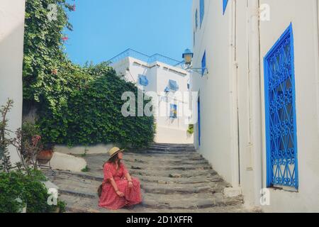 Eine junge Frau sitzt auf der Straße Sidi Bou Said. Haus mit blauen Fenstern und Türen mit arabi Ornamenten, Sidi Bou Said, Tunesien, Afrika Stockfoto
