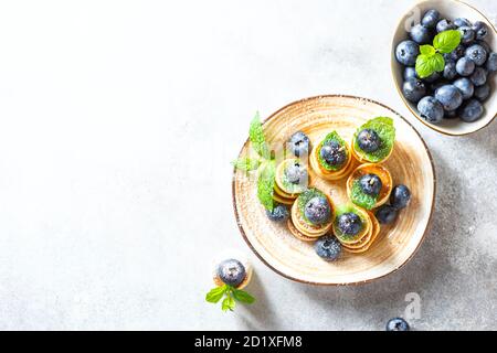 Modisches Essen - Mini-Pfannkuchen mit Heidelbeeren und Minze auf hellem Betongrund. Stockfoto