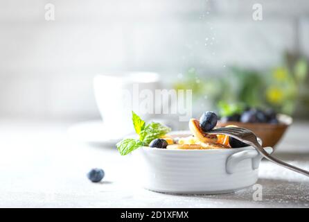 Schüssel mit winzigen Pfannkuchen Müsli auf einem hellen Beton Hintergrund. Trendiges Essen. Mini-Cerealien-Pfannkuchen mit Butter, Honig und Heidelbeeren. Stockfoto