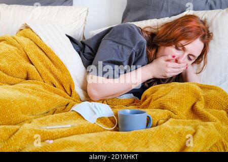 Junge Frau hustet, während sie mit einer Tasse auf dem Bett liegt Tee Stockfoto