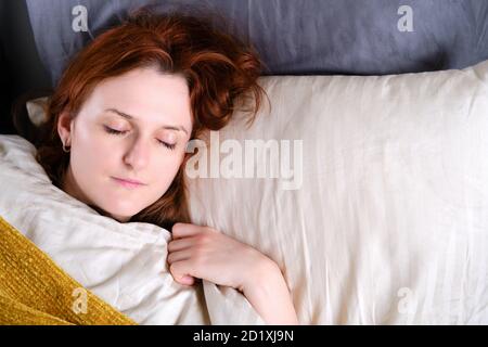 Eine rothaarige Frau schläft auf einem Bett mit einer gelben Decke und weißen Kissen, Platz für Text kopieren Stockfoto