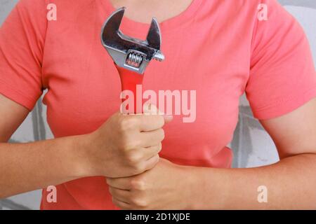 Eine junge Frau mit einem roten Schraubenschlüssel. Ein Werkzeug, um Sanitär selbst zu reparieren. Schraubenschlüssel Nahaufnahme in den Händen der Frauen. Stockfoto