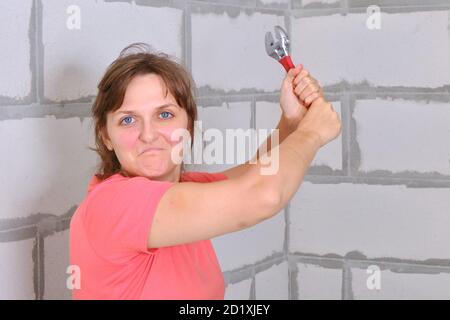 Eine junge Frau schwingt einen roten Schraubenschlüssel. Das Mädchen mit Wut in den Augen bereitet sich auf den Angriff in der Selbstverteidigung. Oder defensiver Angriff mit dem Bauwerkzeug. Stockfoto