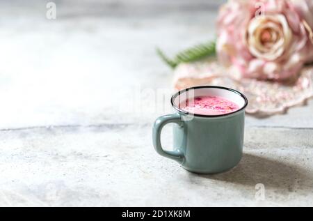 Ayurvedische Rosenmondmilch. Eine trendige, entspannende Form von Getränk vor dem Schlafengehen. Milch mit Rosenblättern in einem grauen Becher auf hellem Betongrund. Stockfoto