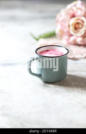 Ayurvedische Rosenmondmilch. Eine trendige, entspannende Form von Getränk vor dem Schlafengehen. Milch mit Rosenblättern in einem grauen Becher auf hellem Betongrund. Stockfoto