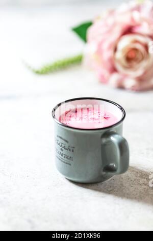 Ayurvedische Rosenmondmilch. Eine trendige, entspannende Form von Getränk vor dem Schlafengehen. Milch mit Rosenblättern in einem grauen Becher auf hellem Betongrund. Stockfoto