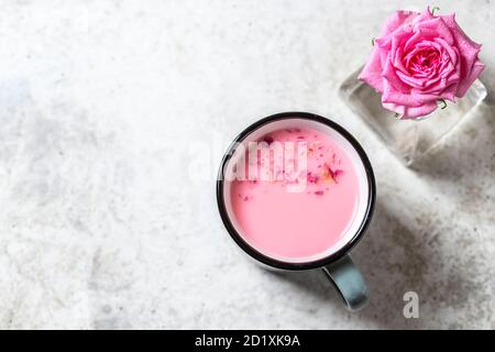 Ayurvedische Rosenmondmilch. Eine trendige, entspannende Form von Getränk vor dem Schlafengehen. Milch mit Rosenblättern in einem grauen Becher auf hellem Betongrund. Stockfoto
