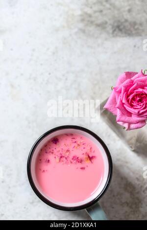 Ayurvedische Rosenmondmilch. Eine trendige, entspannende Form von Getränk vor dem Schlafengehen. Milch mit Rosenblättern in einem grauen Becher auf hellem Betongrund. Stockfoto