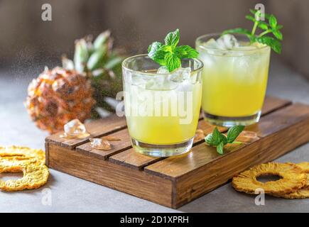 Frisch gepresster Ananassaft mit Ananasscheiben auf hellgrauem Betongrund. Konzept des sommerlichen gesunden Fruchtgetränks. Stockfoto