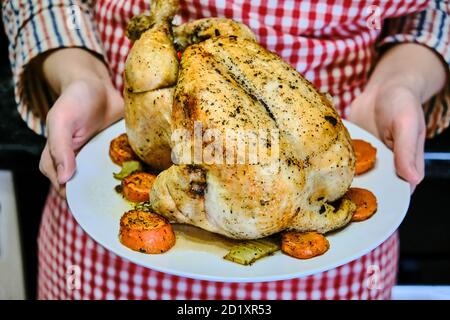 Frauen Hände halten auf einem Teller gegrilltes Huhn. Serviert auf einem festlichen Tisch gebraten. Frau hält ein Gericht mit einem gebackenen Vogel im Ofen. Stockfoto